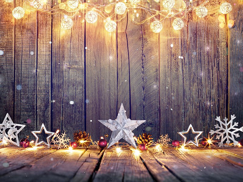 A photograph of festive stars and soft, glowing lights leaning up against a rustic wooden fence.