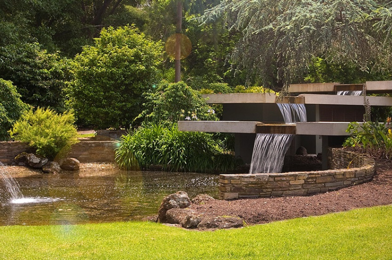 A photograph of a tranquil water feature cascading into a creek, surrounded by lush, green lawns at Springvale Botanical Cemetery.