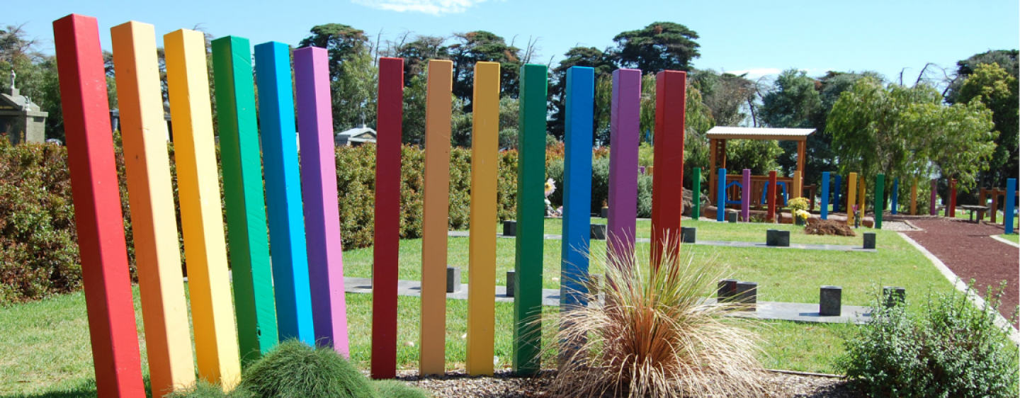 A photograph of a series of pillars in bright colours, forming a bright rainbow sculpture at Bunurong Memorial Park's Avenue of Rainbows