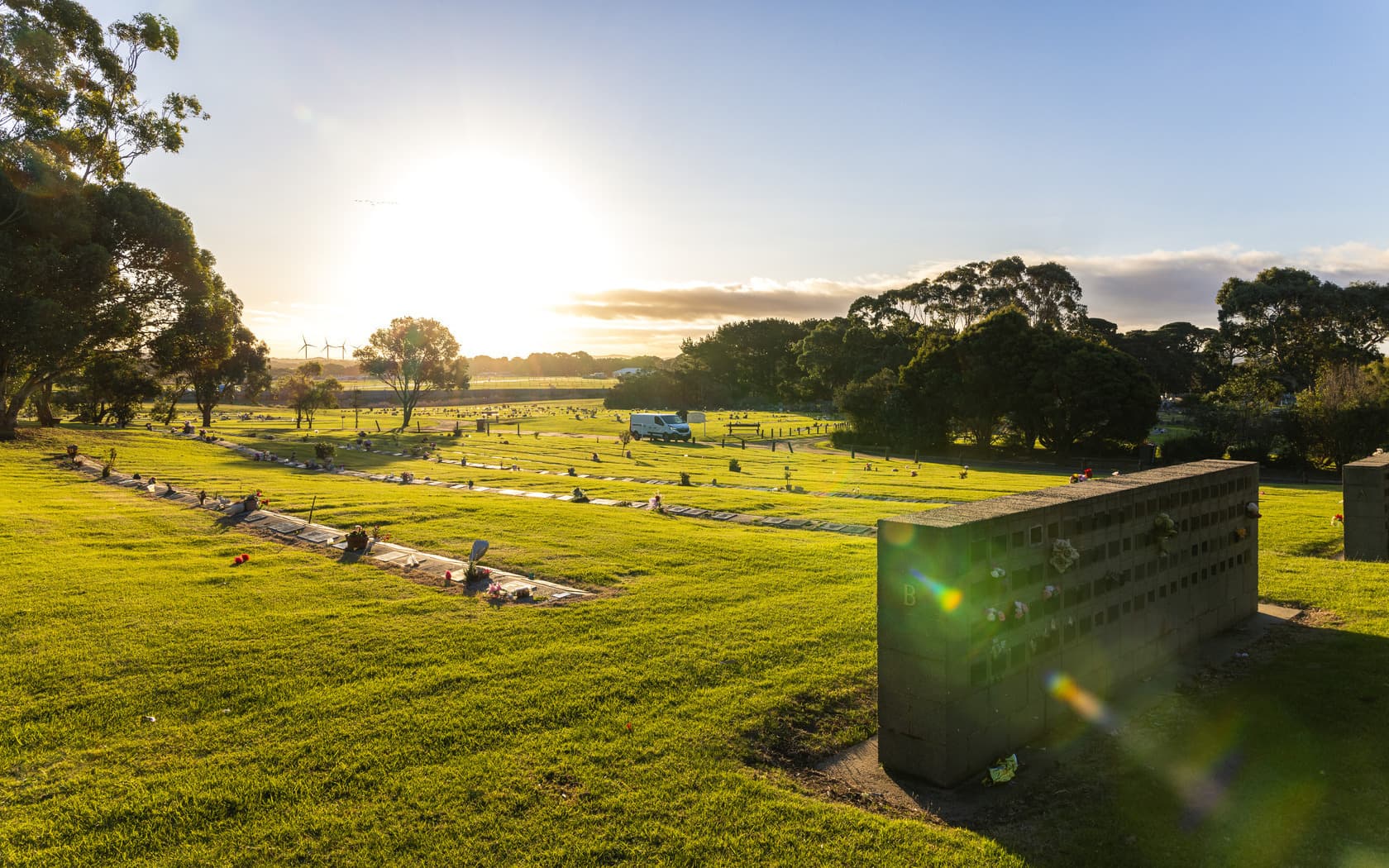 Neat rows of lawn graves set in vast green lawn with a sunset view.