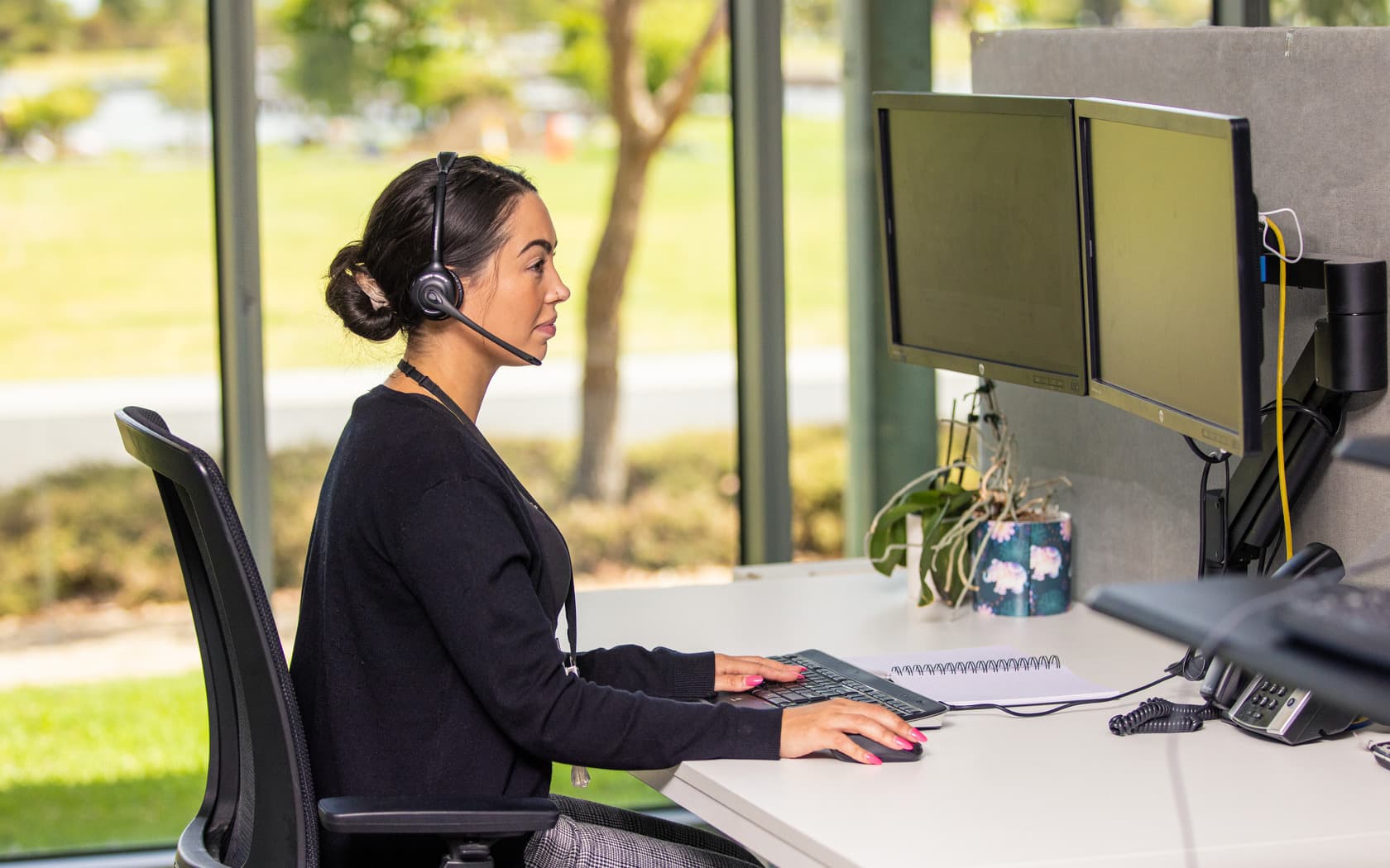 Call centre staff member taking a customer call while working on a computer in a professional office environment