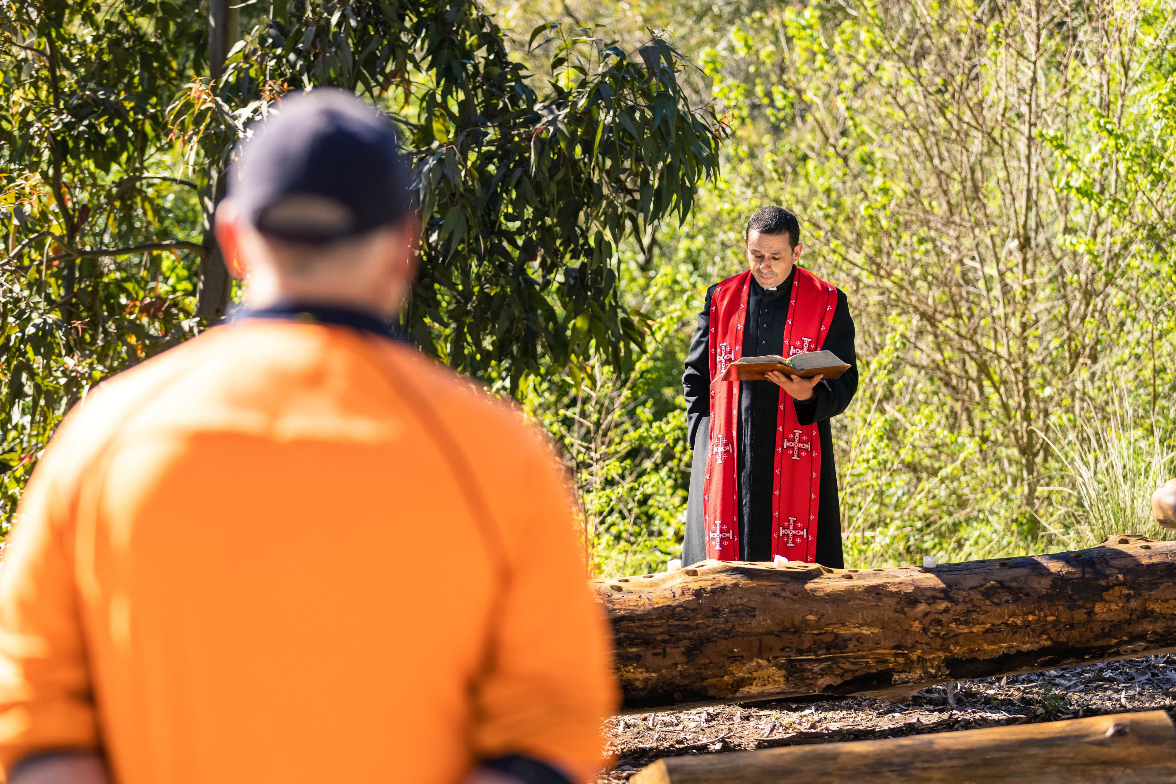 A priest offering a blessing over a handmade All Souls’ Day reflection installation crafted from reclaimed tree branches, symbolising remembrance and renewal.